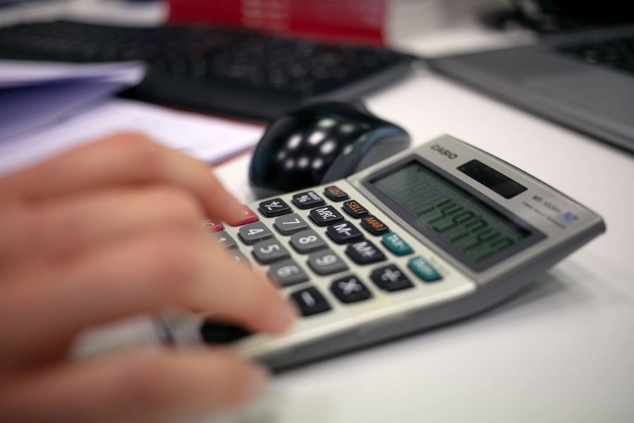 Mão operando uma calculadora sobre a mesa de trabalho