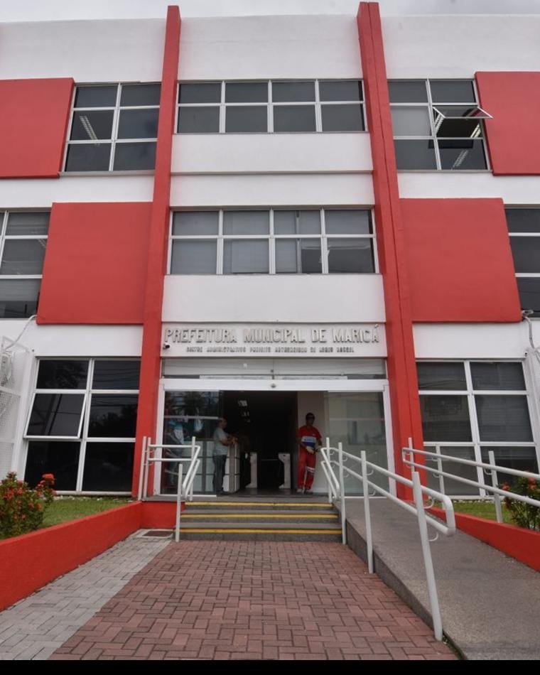 Prédio de três andares em faixas vermelhas e brancas, com rampa de acesso e o letreiro da Prefeitura sobre a entrada